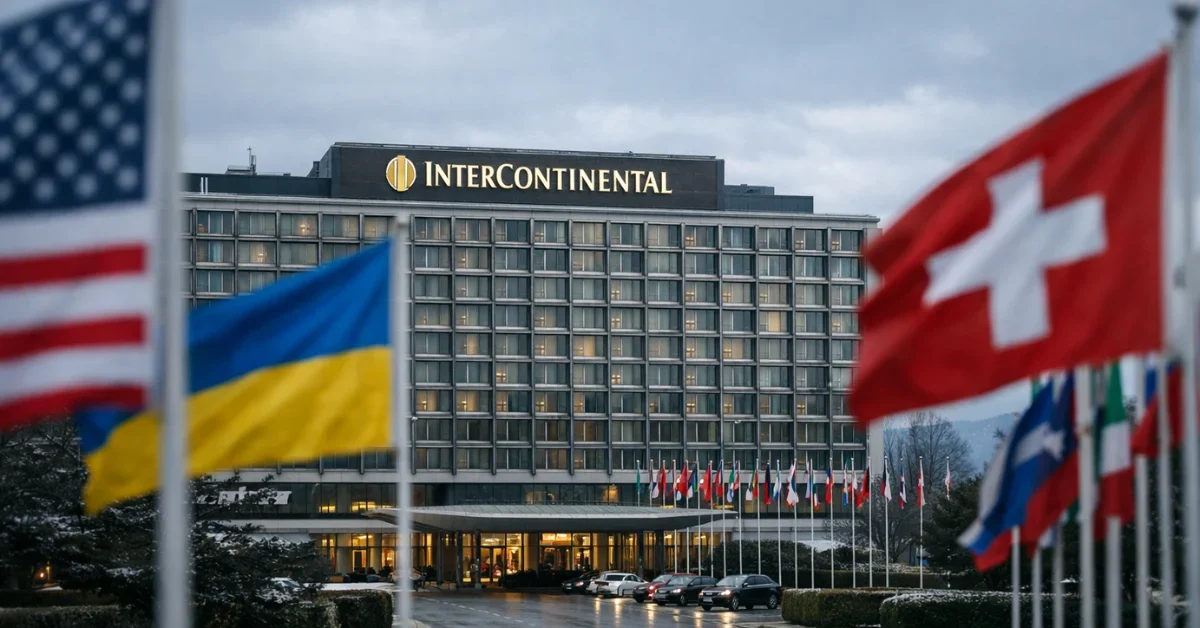 The exterior of the Intercontinental Hotel in Geneva, Switzerland, where peace talks are held, featuring international flags in the foreground under a cloudy winter sky.