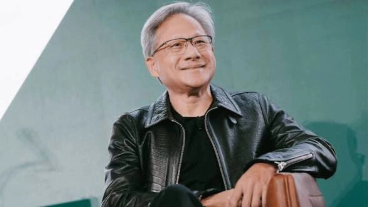 Nvidia CEO Jensen Huang wearing a black leather jacket on stage at a technology conference, presenting new AI hardware to a large audience in a dimly lit auditorium.