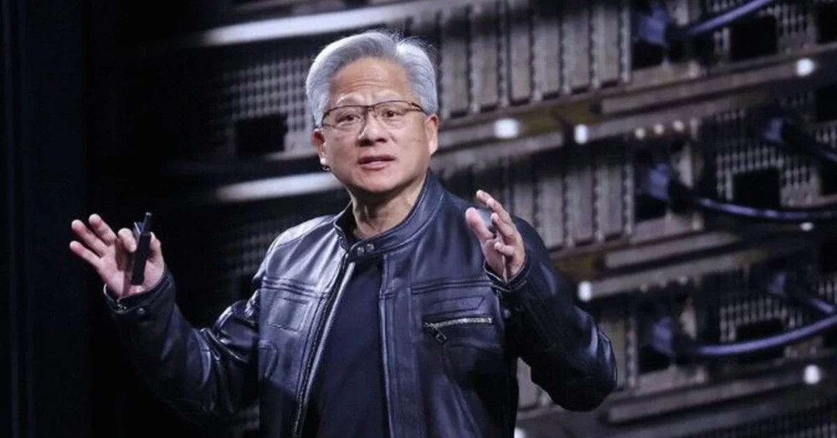 Nvidia CEO Jensen Huang speaking on a conference stage with AI chip graphics on a large screen and an audience in the foreground.