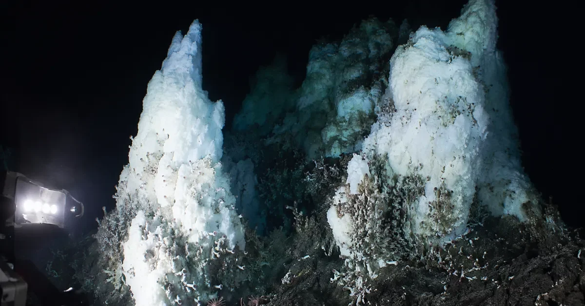 Underwater view of towering frozen methane ice structures illuminated by submarine lights in the deep ocean.