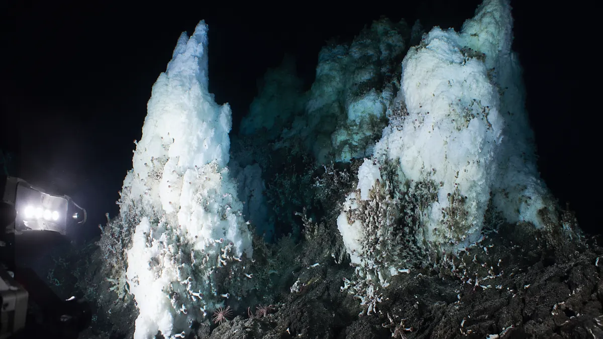Underwater view of towering frozen methane ice structures illuminated by submarine lights in the deep ocean.